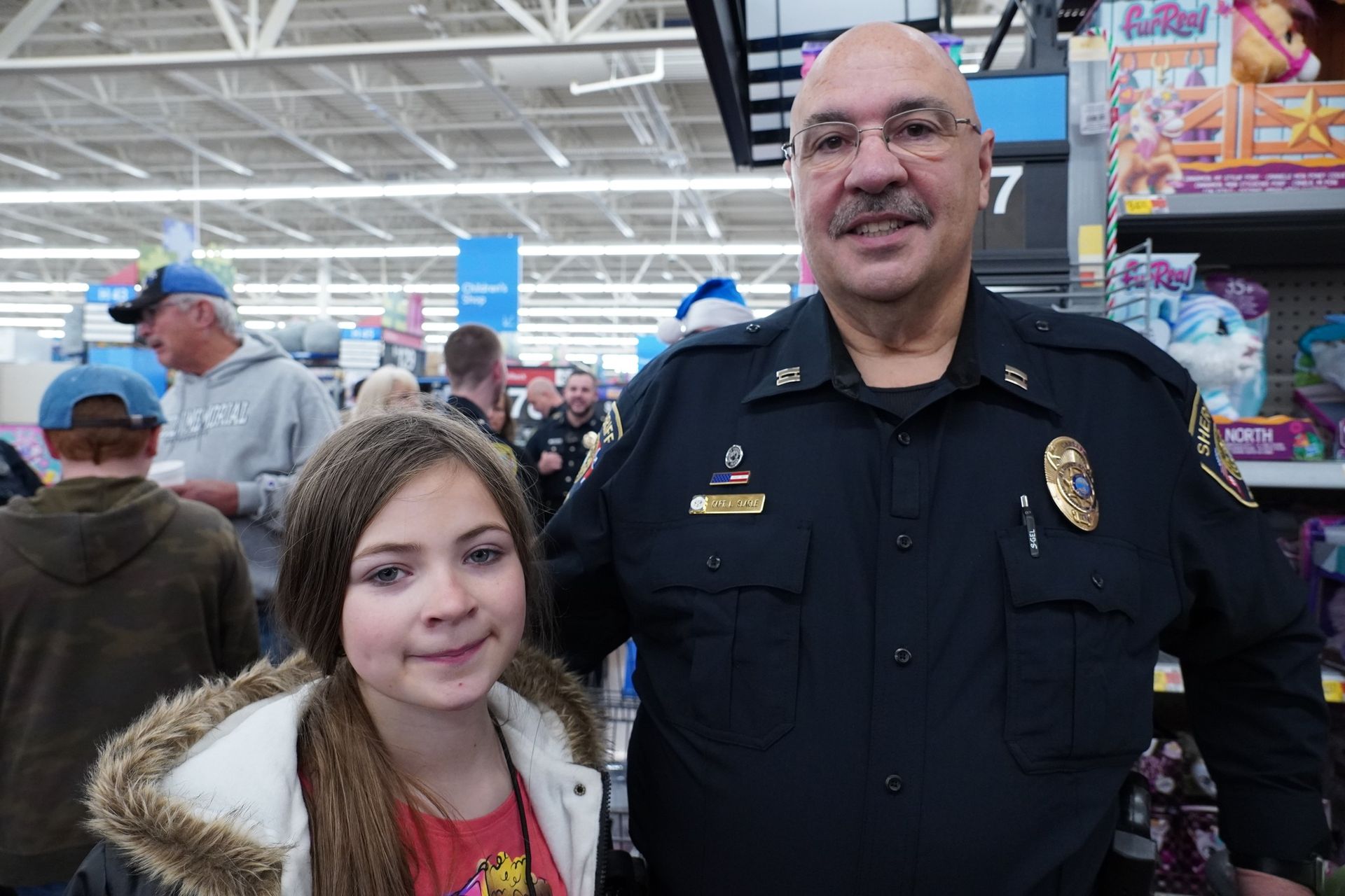 A police officer is posing for a picture with a young girl in a store.