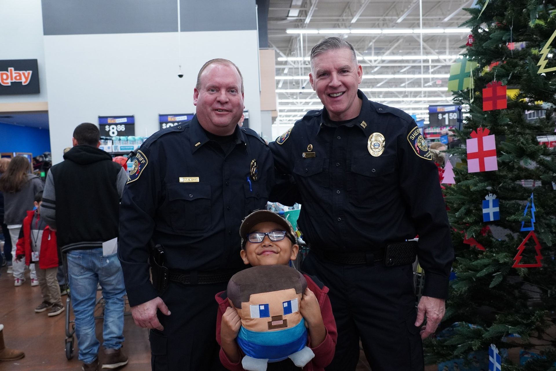 Two police officers are posing for a picture with a child in front of a christmas tree.