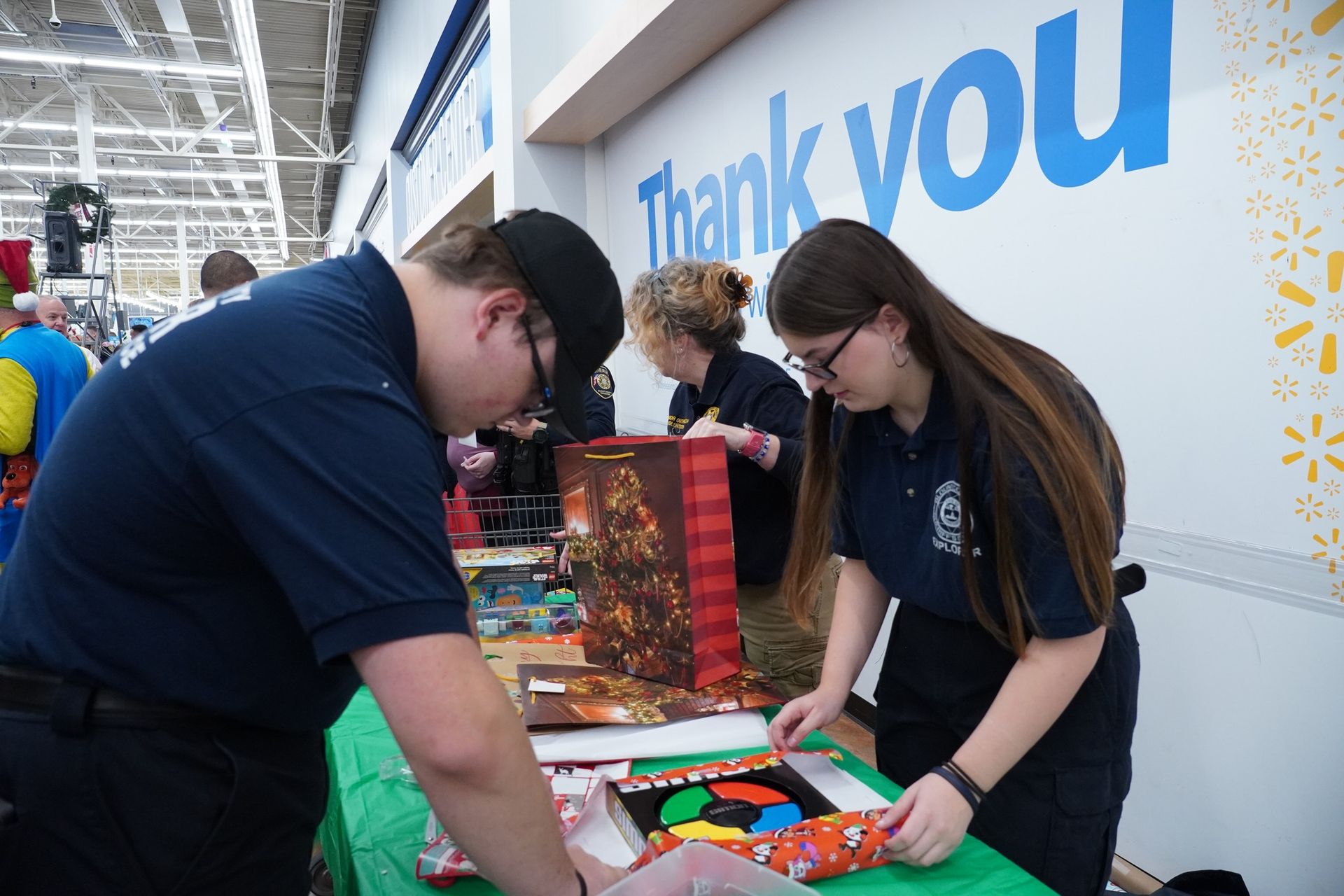 A man and a woman are wrapping gifts in front of a thank you sign.