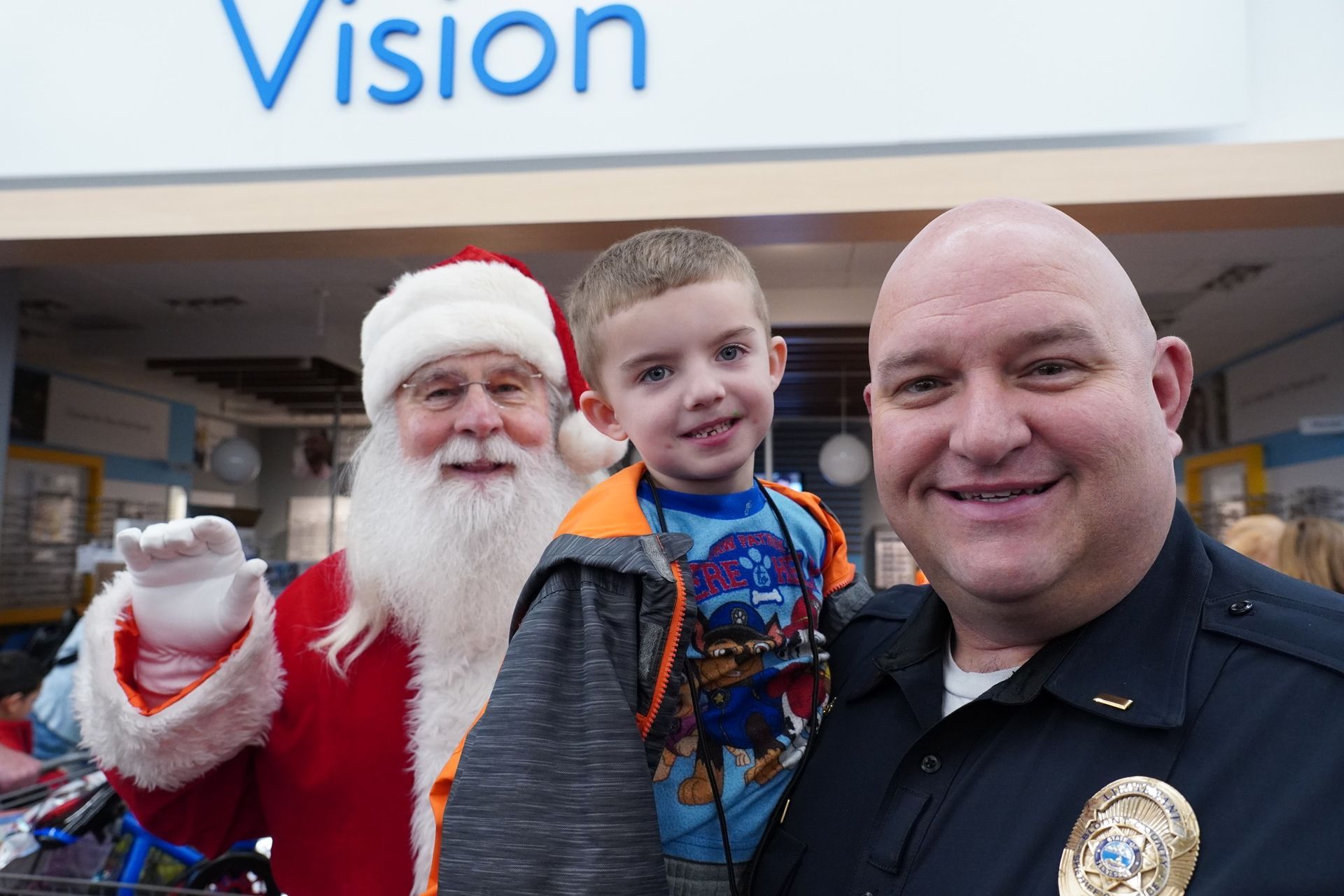 A police officer is holding a young boy next to santa claus.