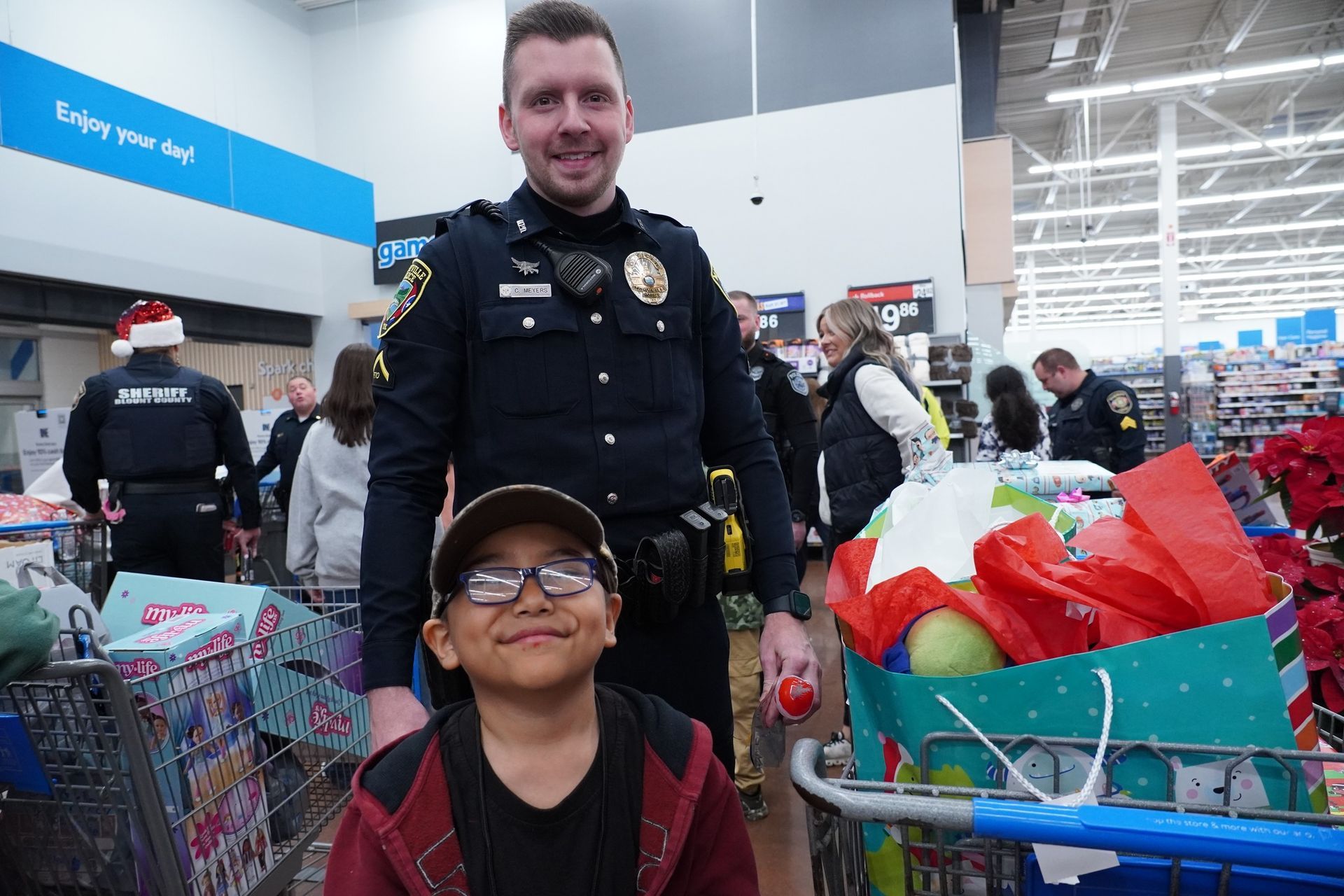 A police officer standing with little boy and shopping cart full of toys.