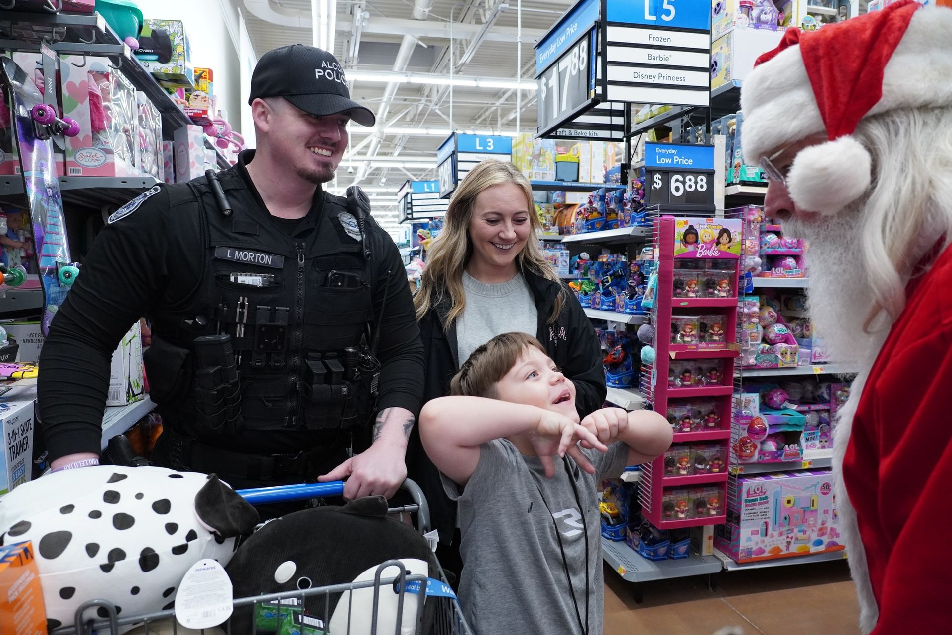 A police officer shopping with little boy and a lady who looks to be his mother talking to Santa Claus.