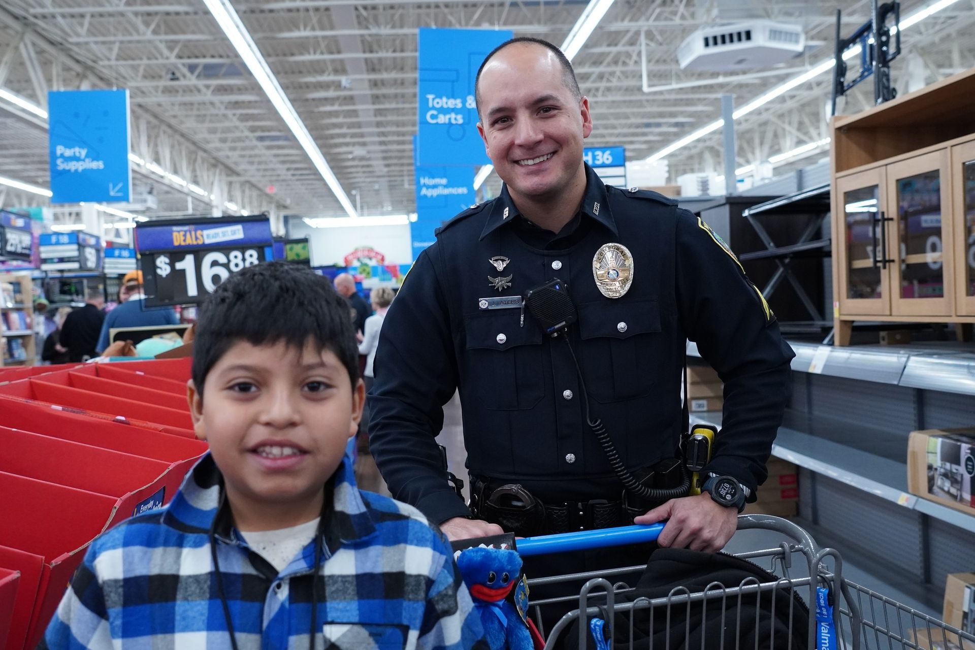 A police officer is standing next to a boy in a shopping cart.