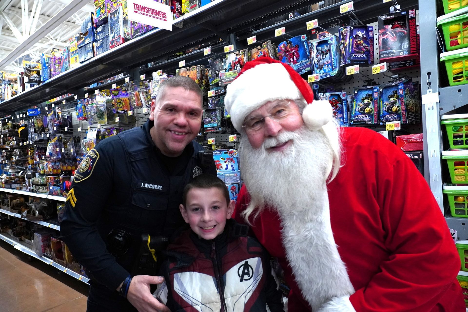 A police officer and a little boy are posing for a picture with santa claus in a store.