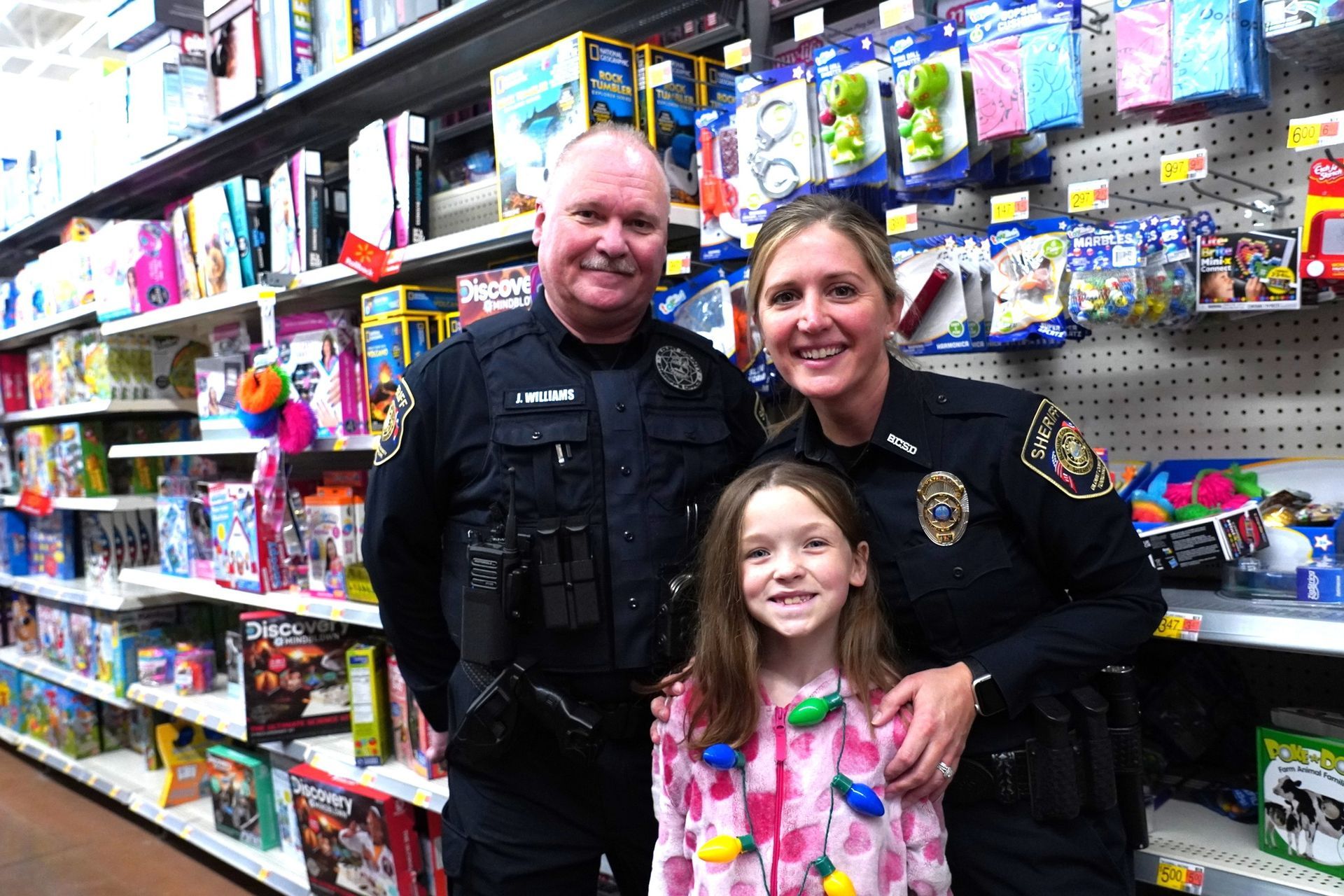 Two police officers and a little girl are posing for a picture in a store.
