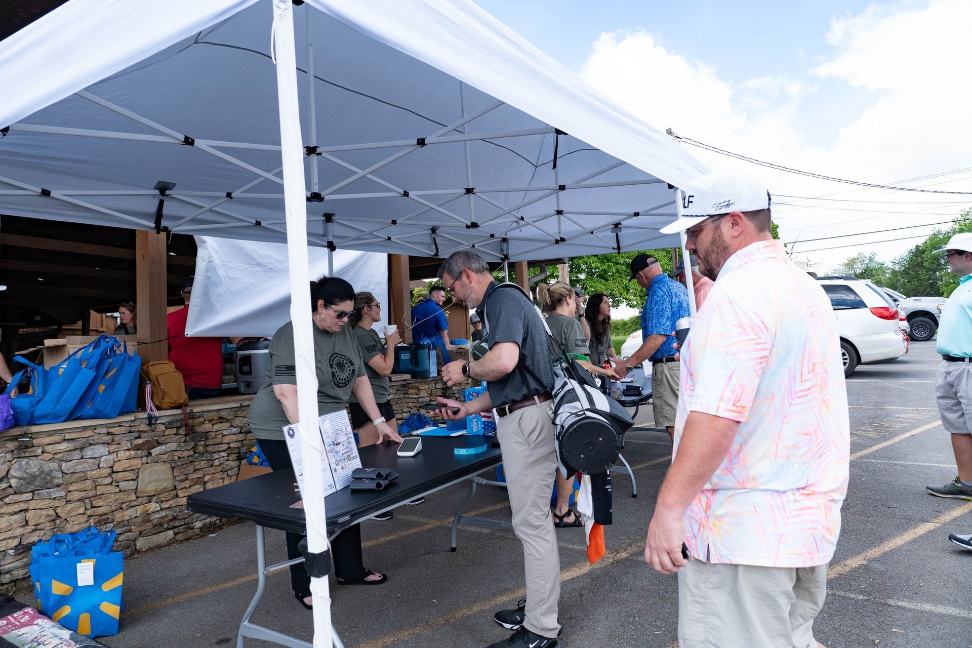 A group of people are standing under a tent in a parking lot.