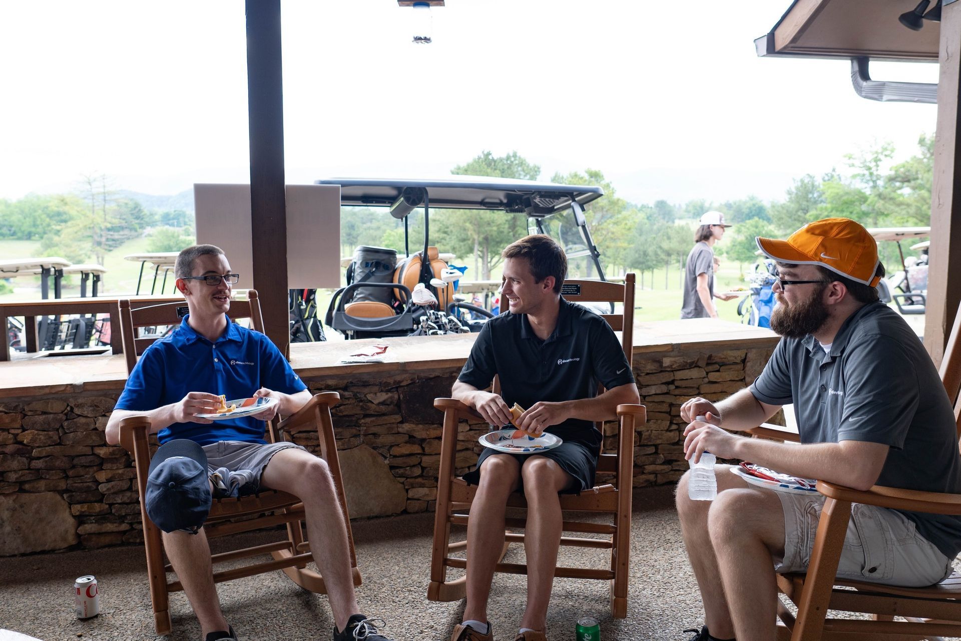 Three men are sitting in rocking chairs on a porch with a golf cart in the background.