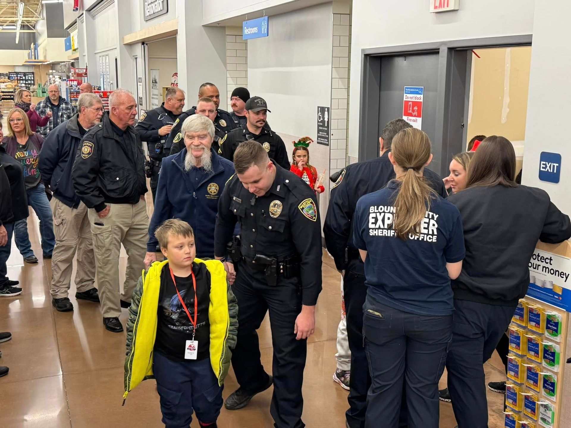A group of police officers and a boy are walking through a store.