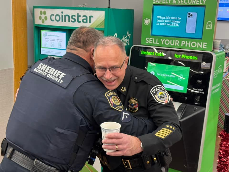 Two police officers hugging in front of a coinstar vending machine