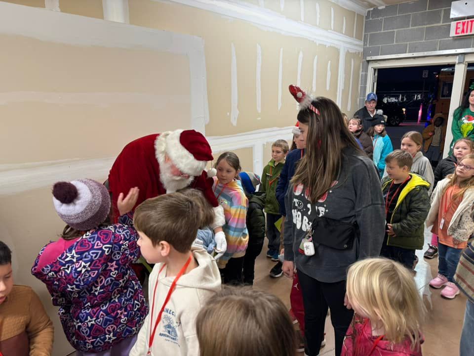 A group of children are standing in a hallway talking to santa claus.