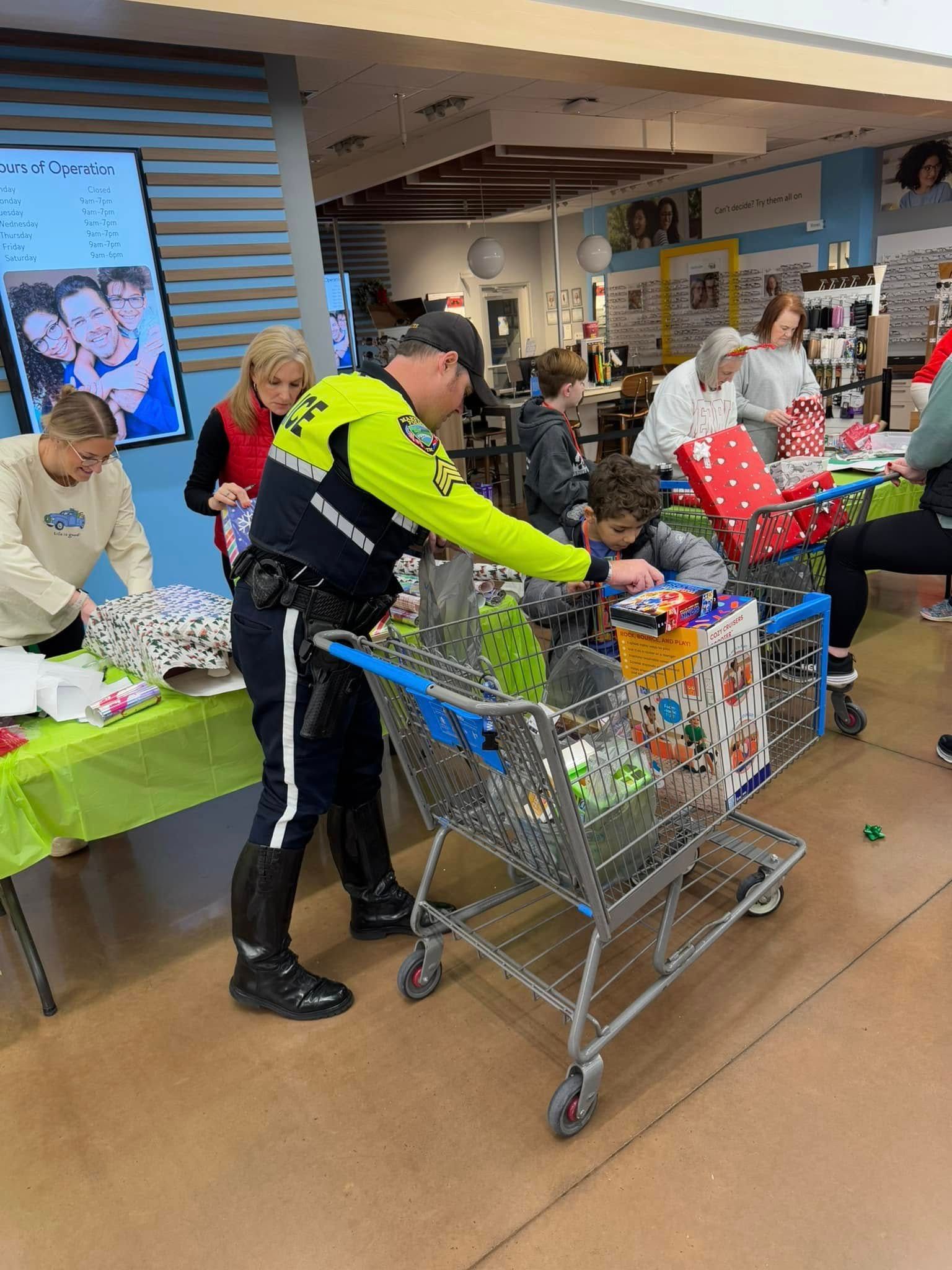A police officer is pushing a shopping cart full of gifts in a store.