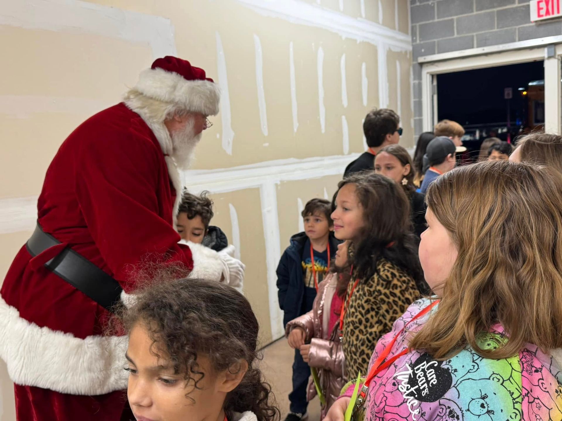 A group of children are standing in a room talking to santa claus.
