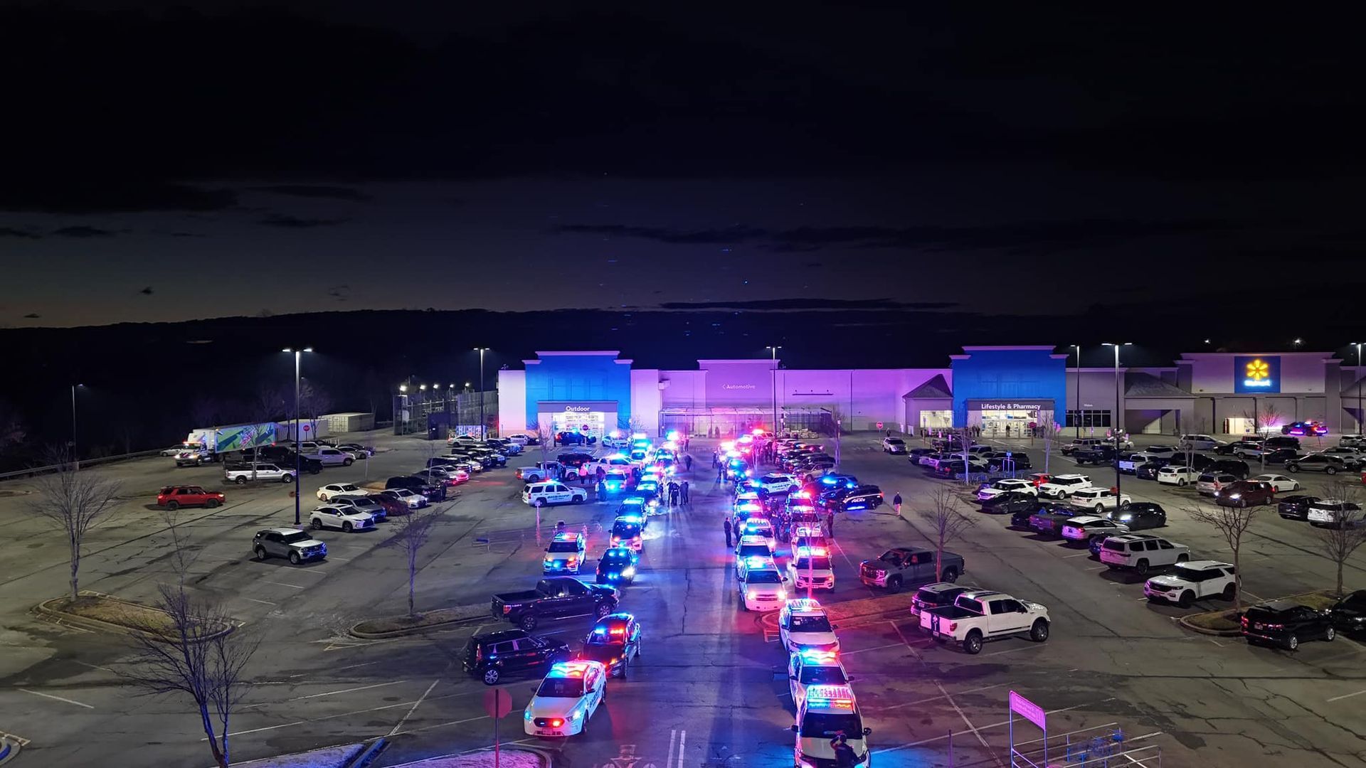 An aerial view of a parking lot filled with cars and police cars at night.