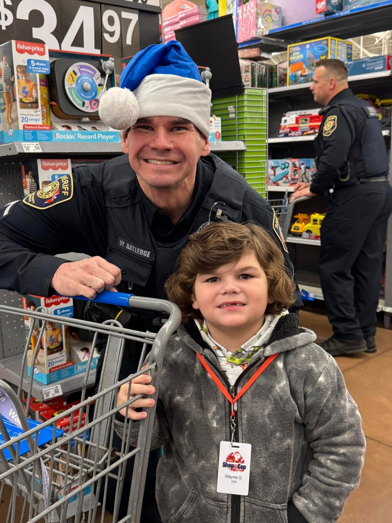 A man in a santa hat is standing next to a boy in a shopping cart.