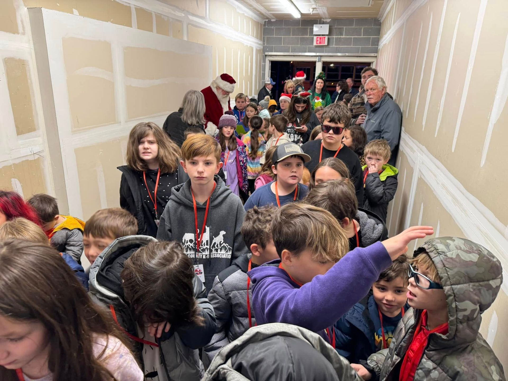 A group of children are standing in a hallway with santa claus.