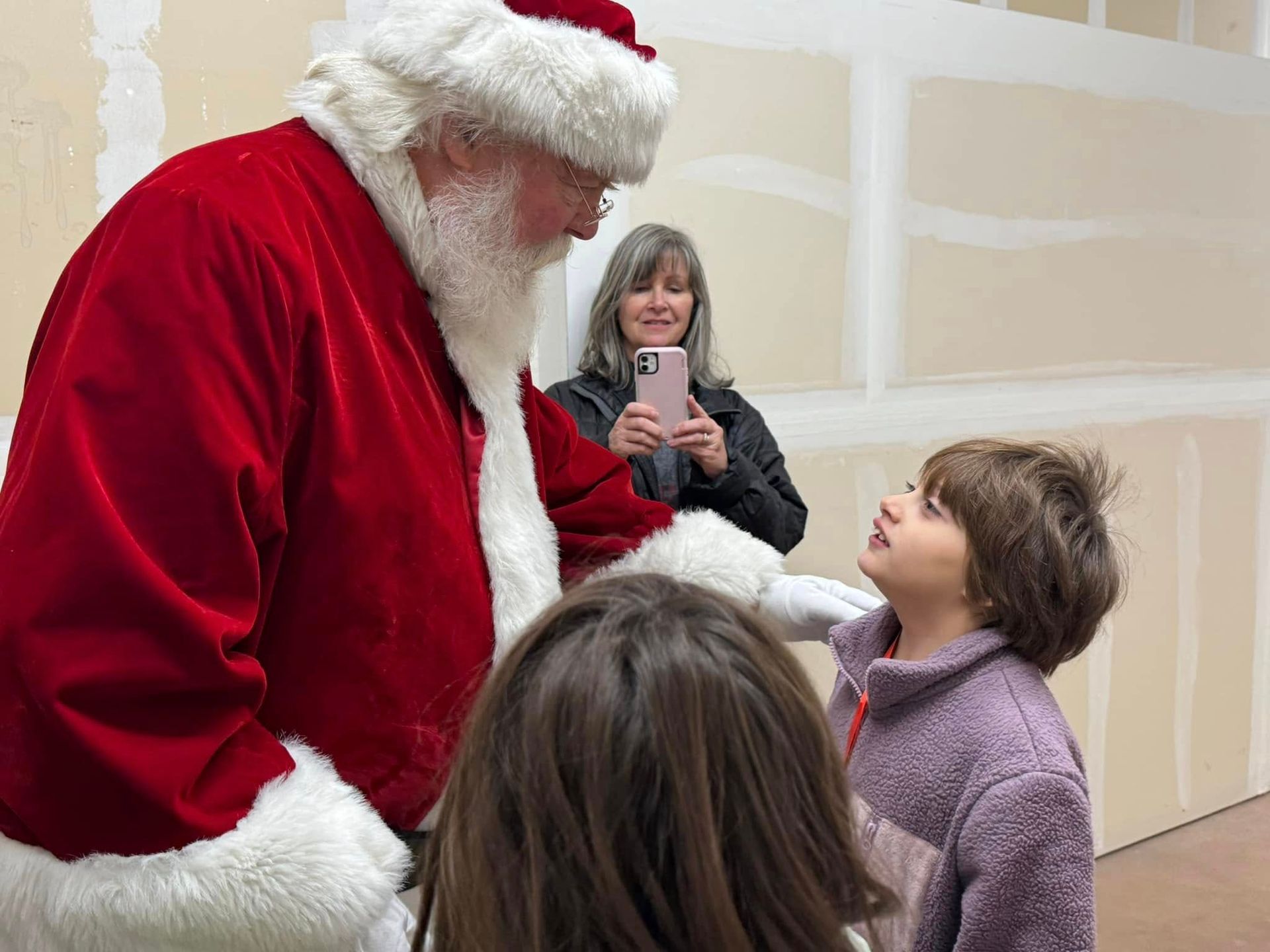 A woman is taking a picture of a child talking to santa claus.