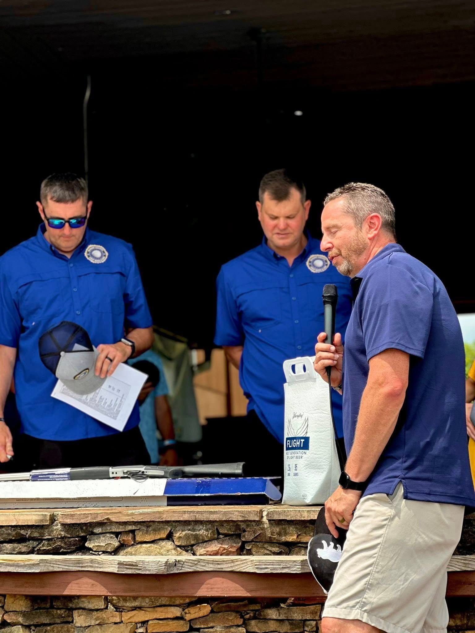 A man is holding a microphone in front of a group of men in blue shirts.
