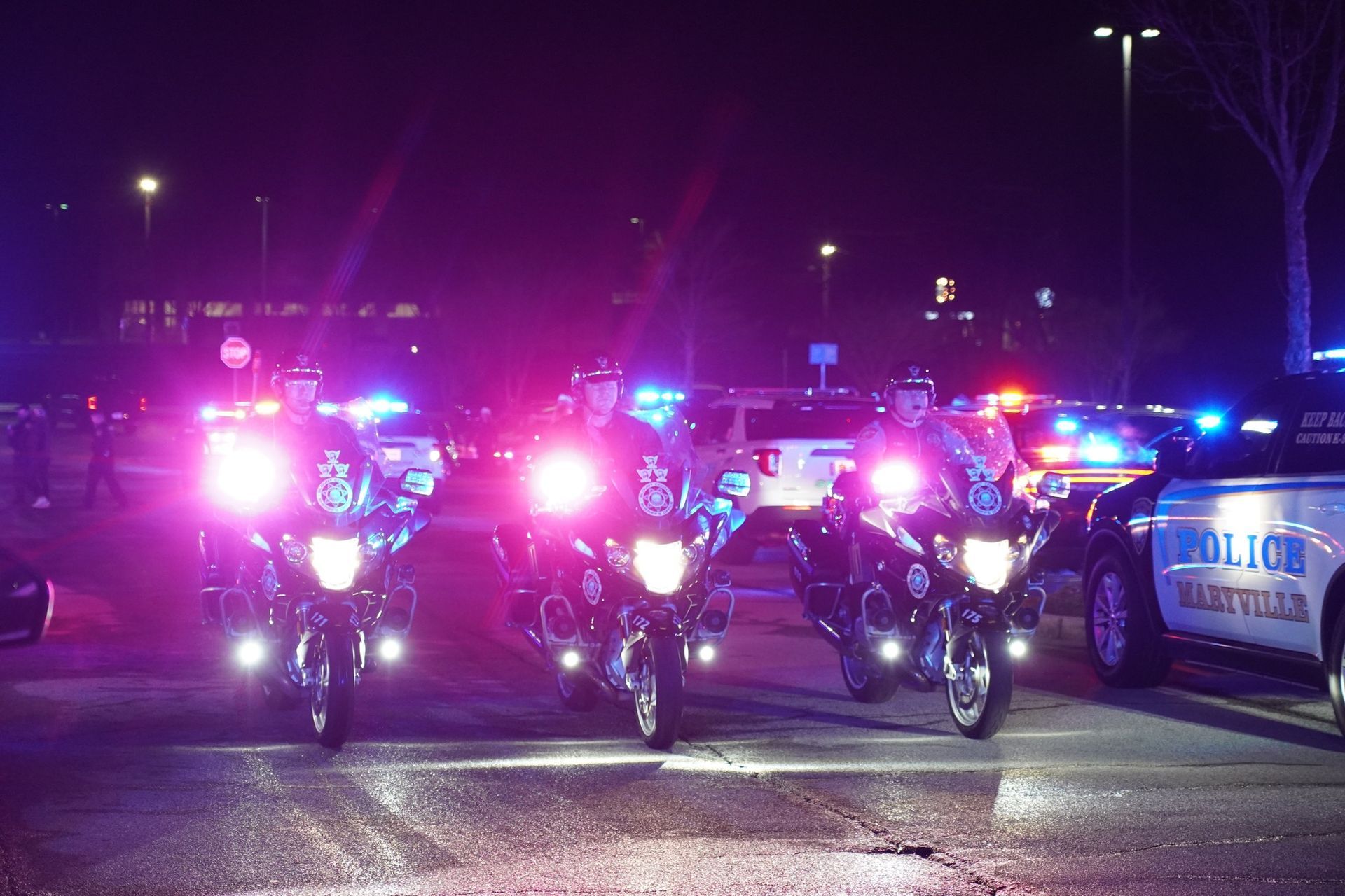 Police motorcycles and patrol cars with flashing lights at night.