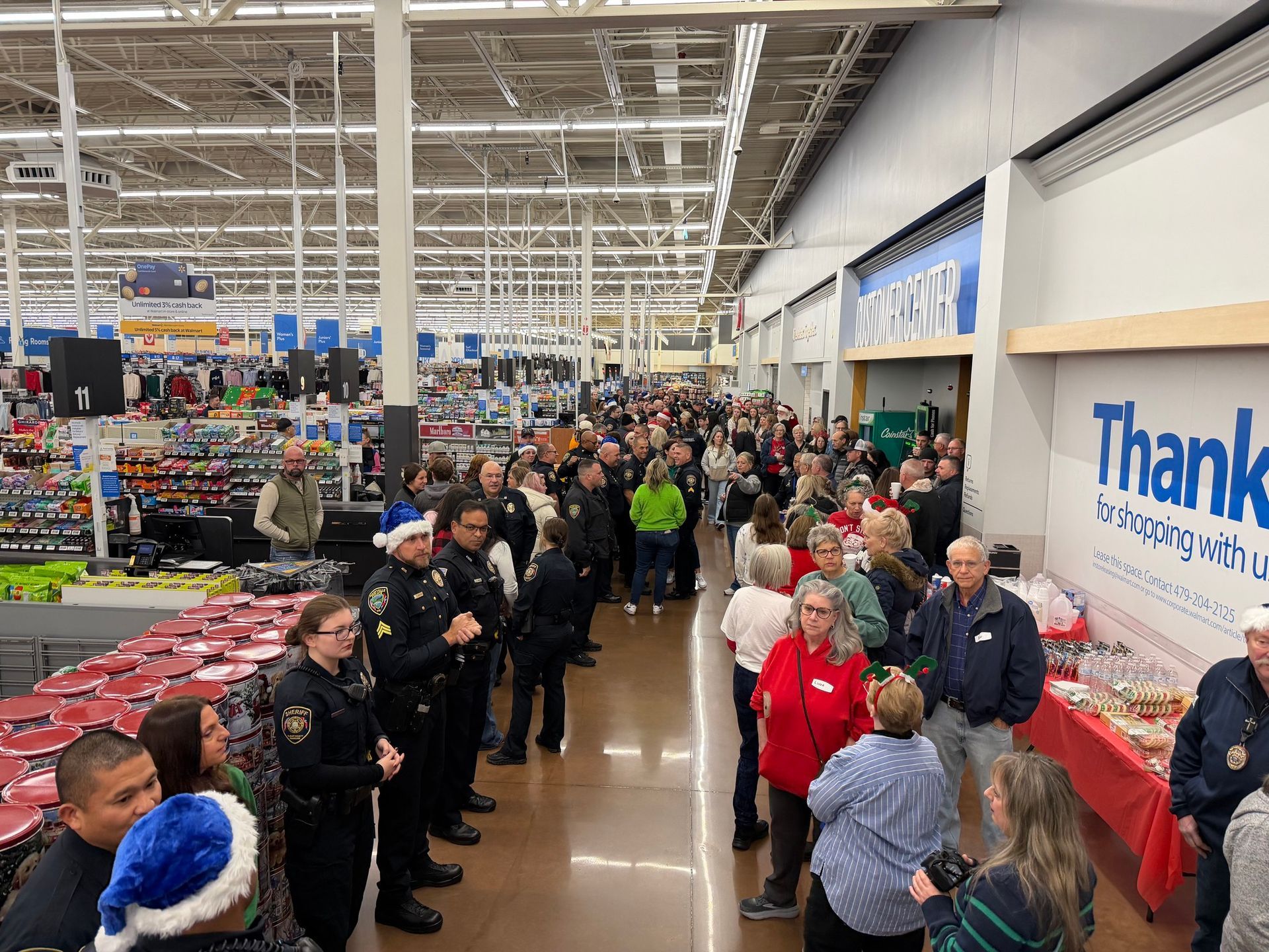 Large crowd in a Walmart, with police officers, tables of food, and Christmas decorations.
