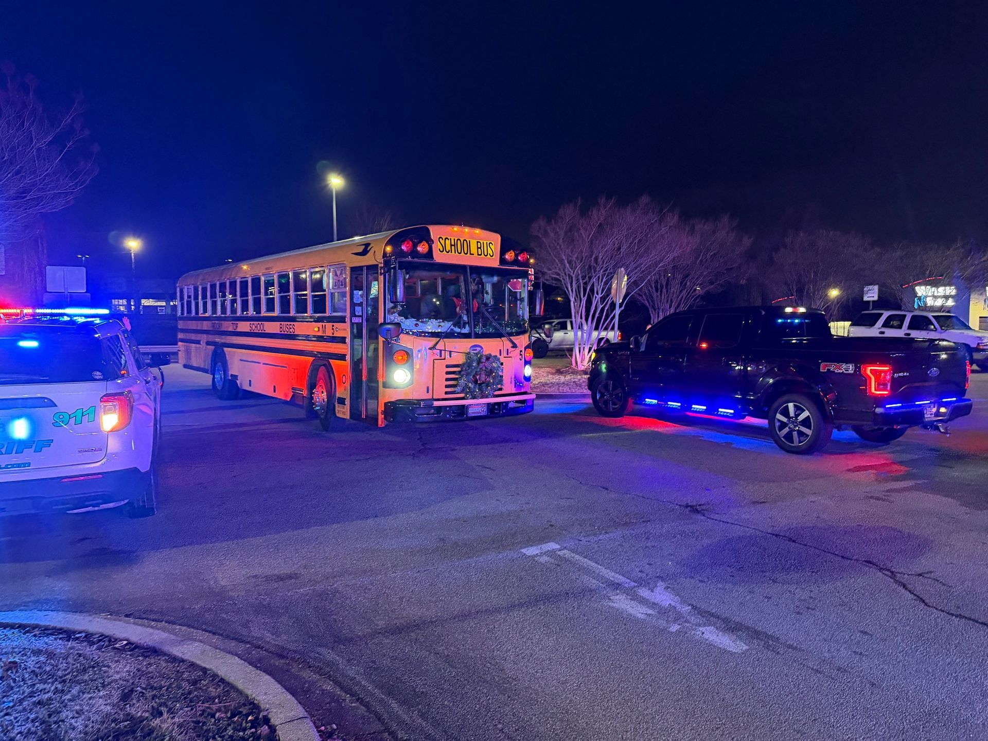 School bus and black pickup truck stopped with police car lights flashing at night.