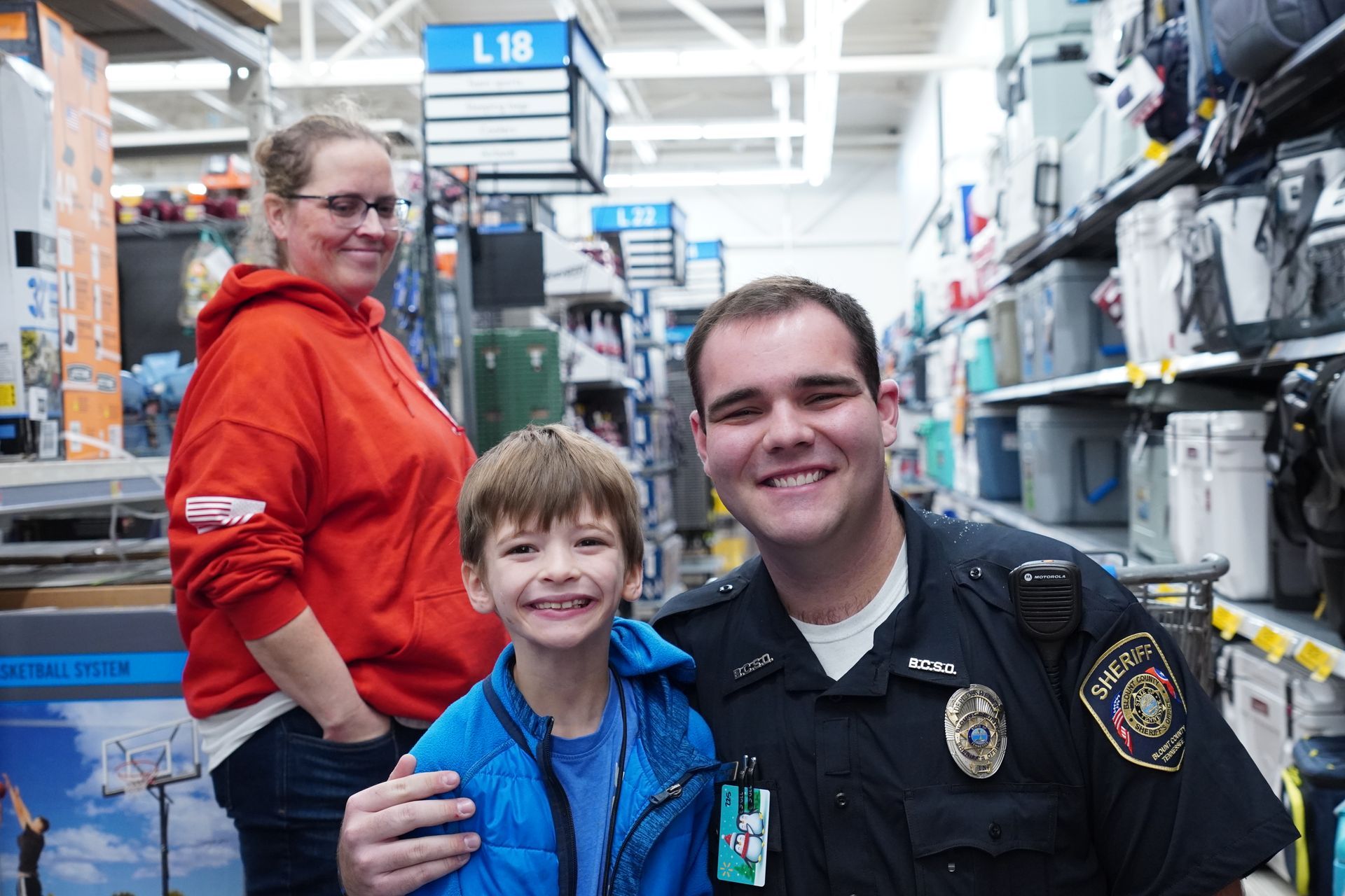 A police officer is posing for a picture with a boy and a woman in a store.