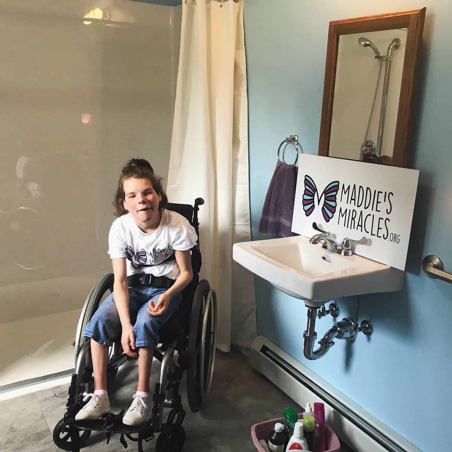 A girl in a wheelchair in a bathroom with a sign that says maddie 's miracles