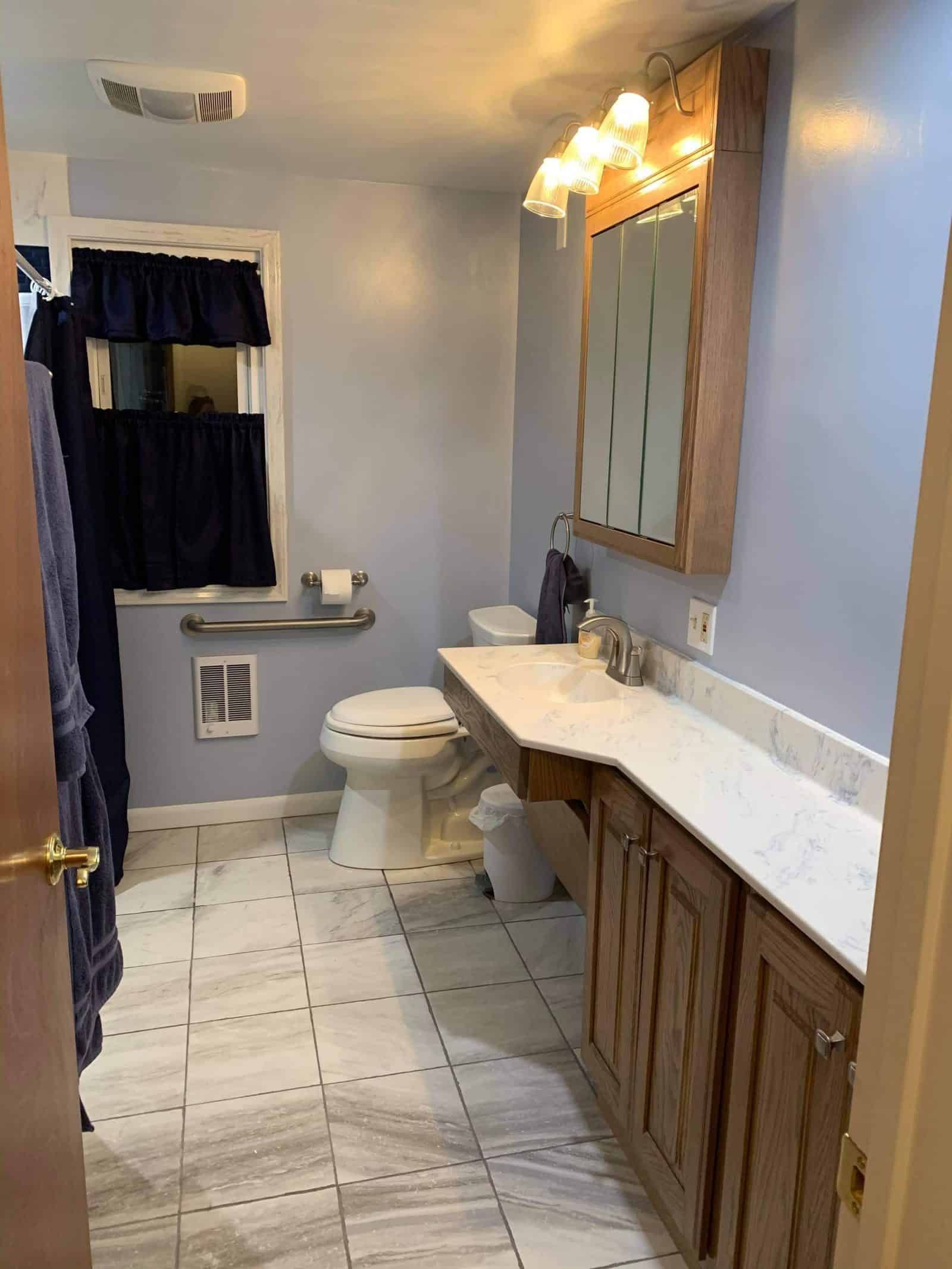 Bathroom with light blue walls, wood vanity, and white tile floor.