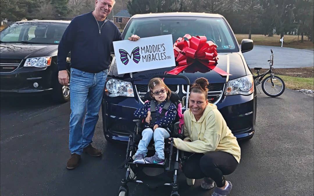 A little girl in a wheelchair is sitting in front of a car.