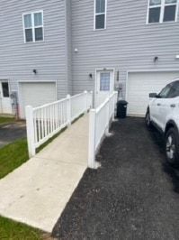 Exterior view of a townhome with a concrete ramp and white railing for accessibility. Gray siding.