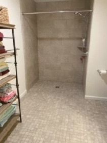 Spacious accessible shower with tiled walls and floor, glass door, and a chrome showerhead in a neutral-toned bathroom.