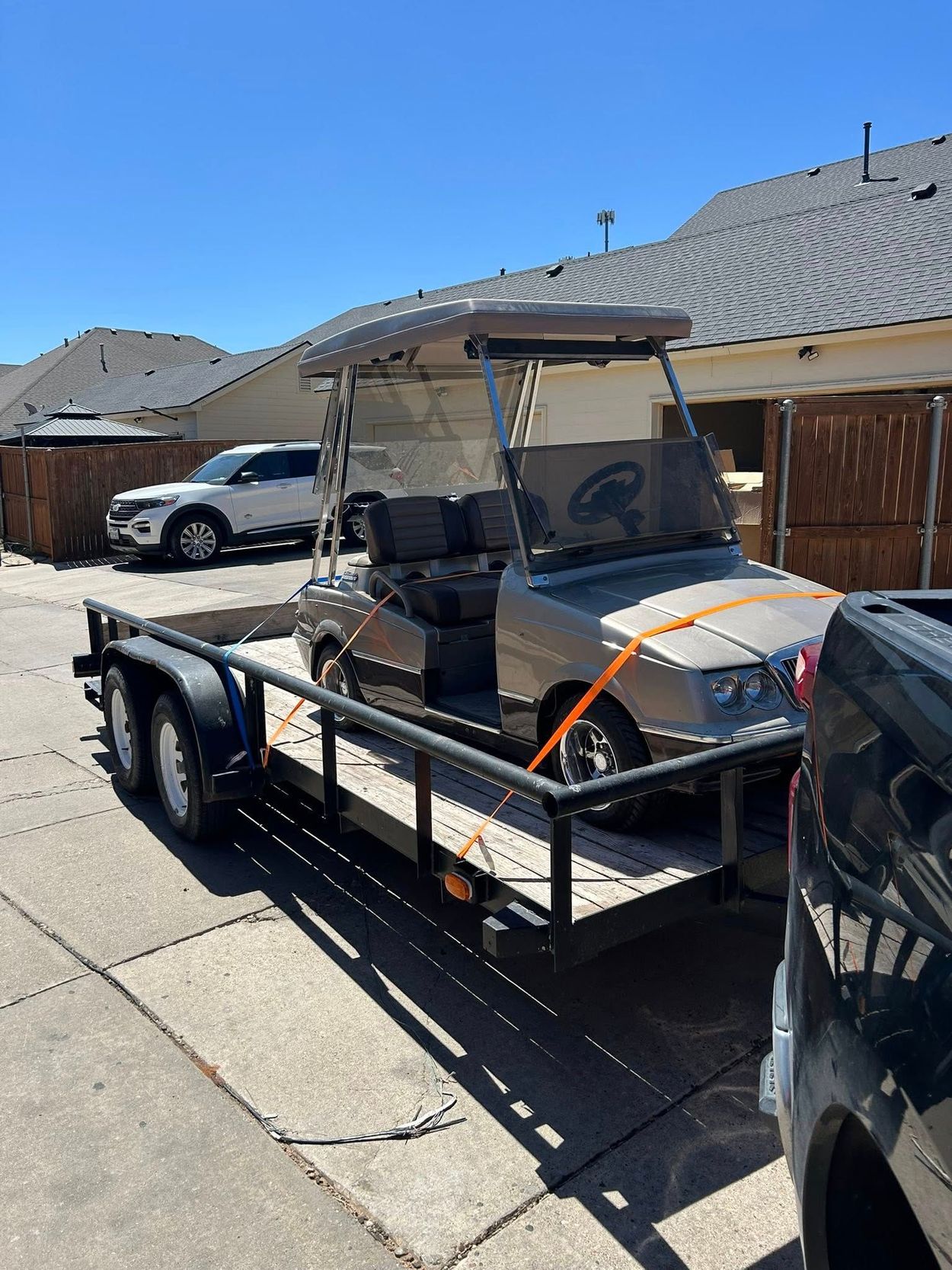 Golf cart secured on a trailer outdoors on a sunny day.