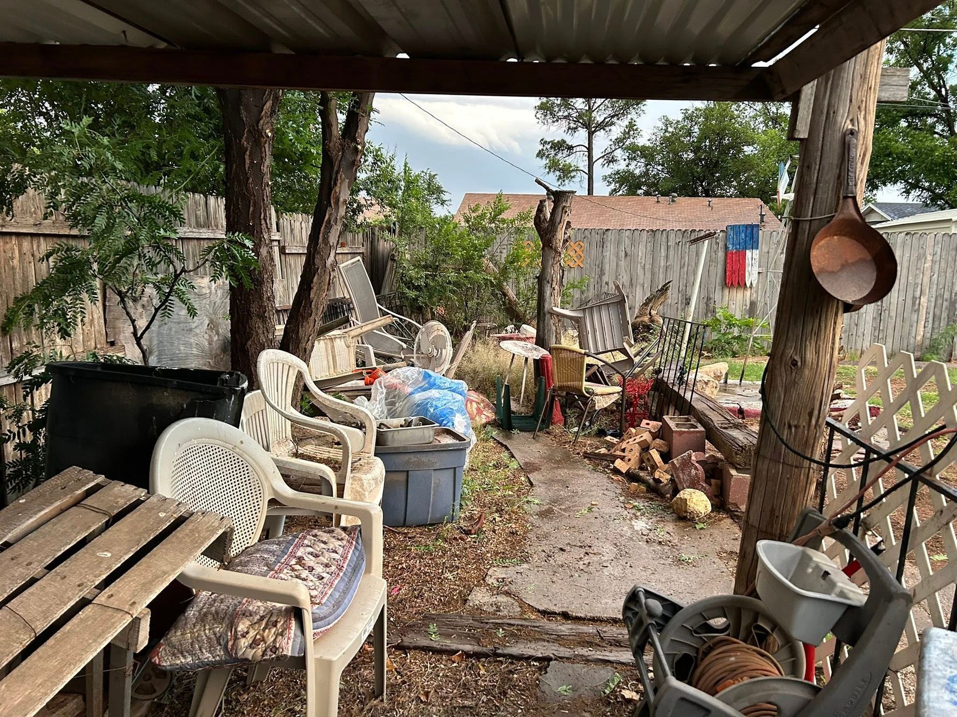 Backyard scene with patio furniture and storage amid trees and fence.