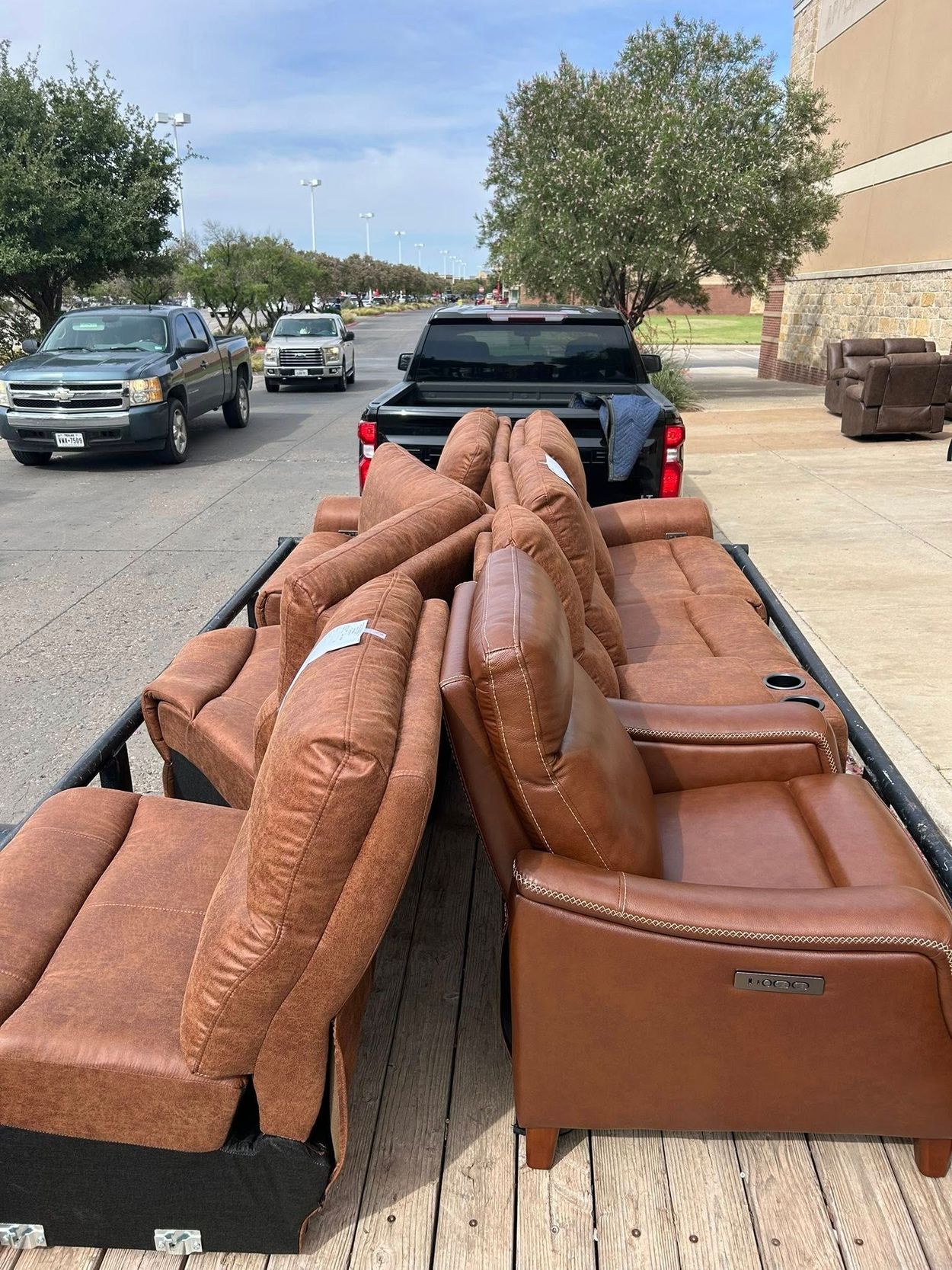 Brown leather sectional sofa loaded on a trailer, backed by a black pickup truck on a street.