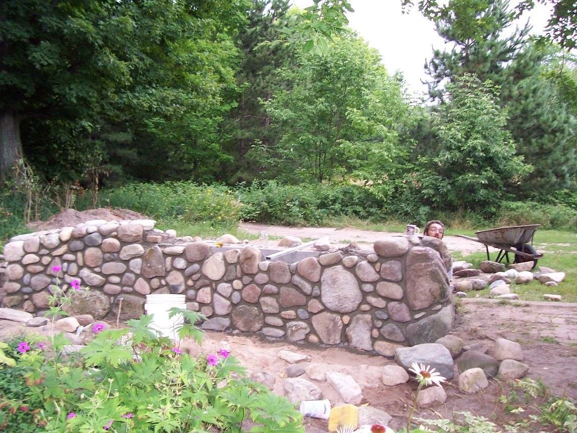 A stone wall is being built in a garden with trees in the background.