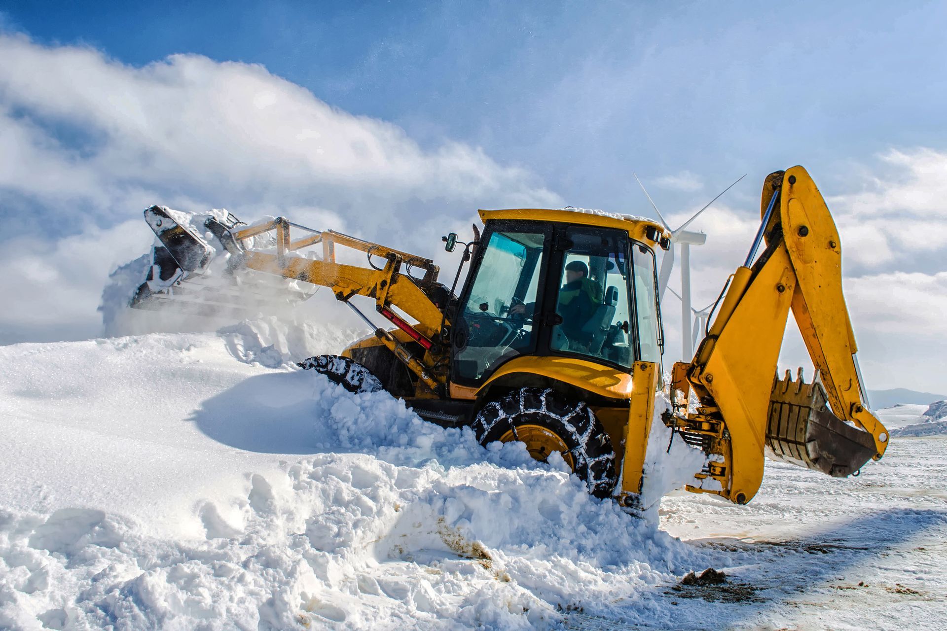 A yellow excavator is clearing snow from a snowy field.