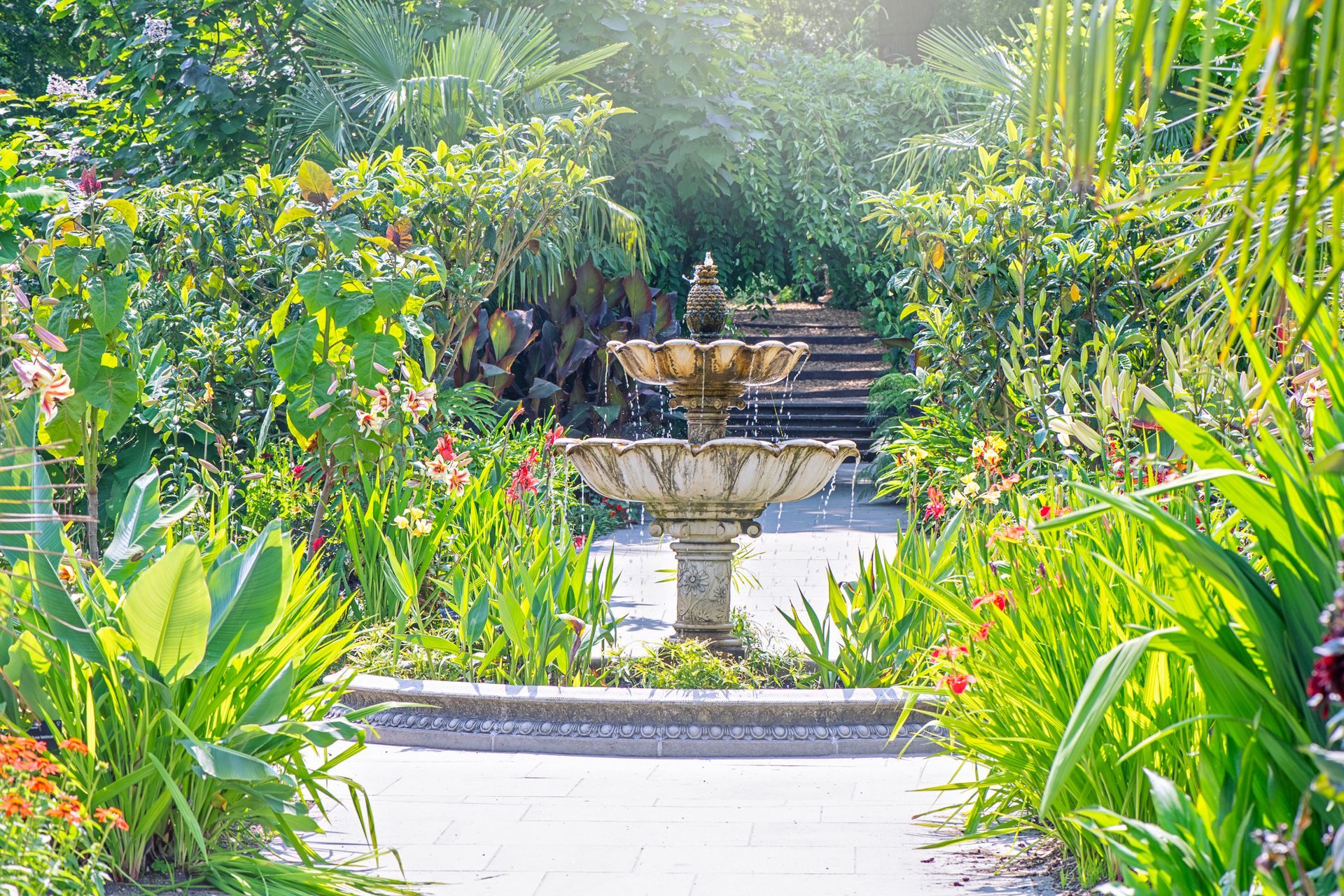 There is a fountain in the middle of a garden surrounded by flowers.