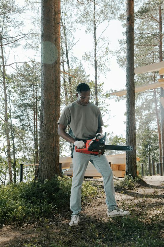 A man is standing in the woods holding a chainsaw.