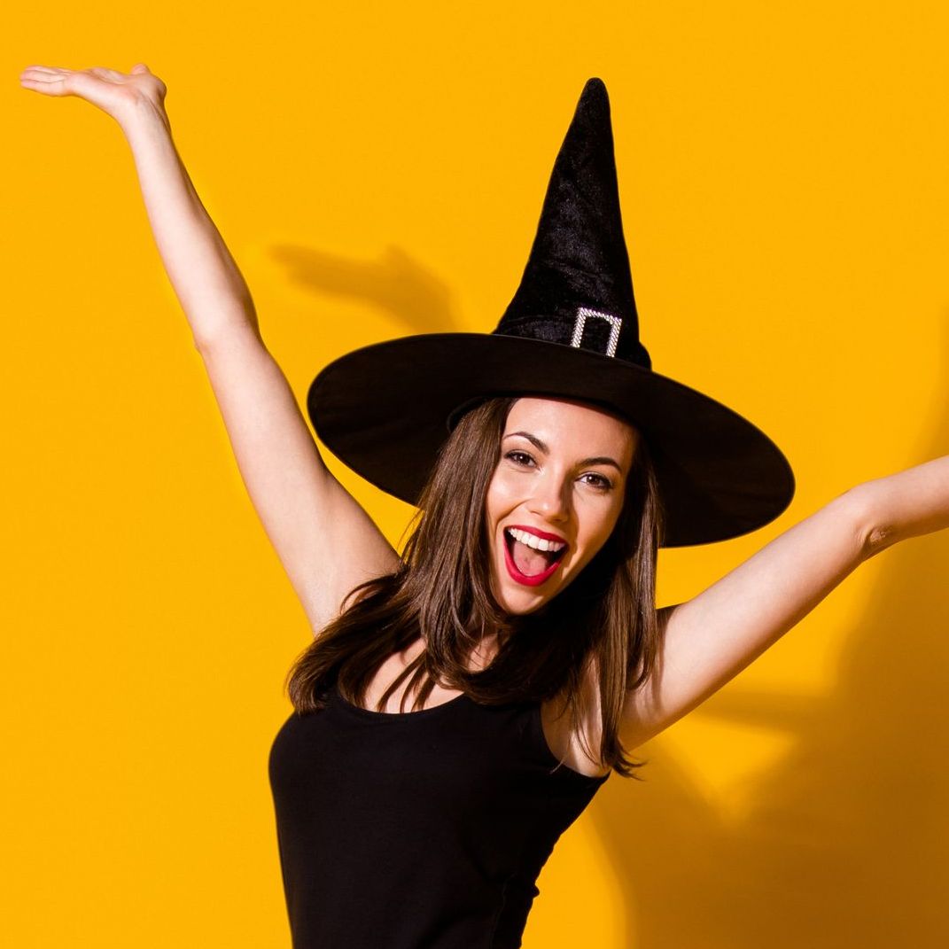 A woman wearing a black witch hat with her arms outstretched