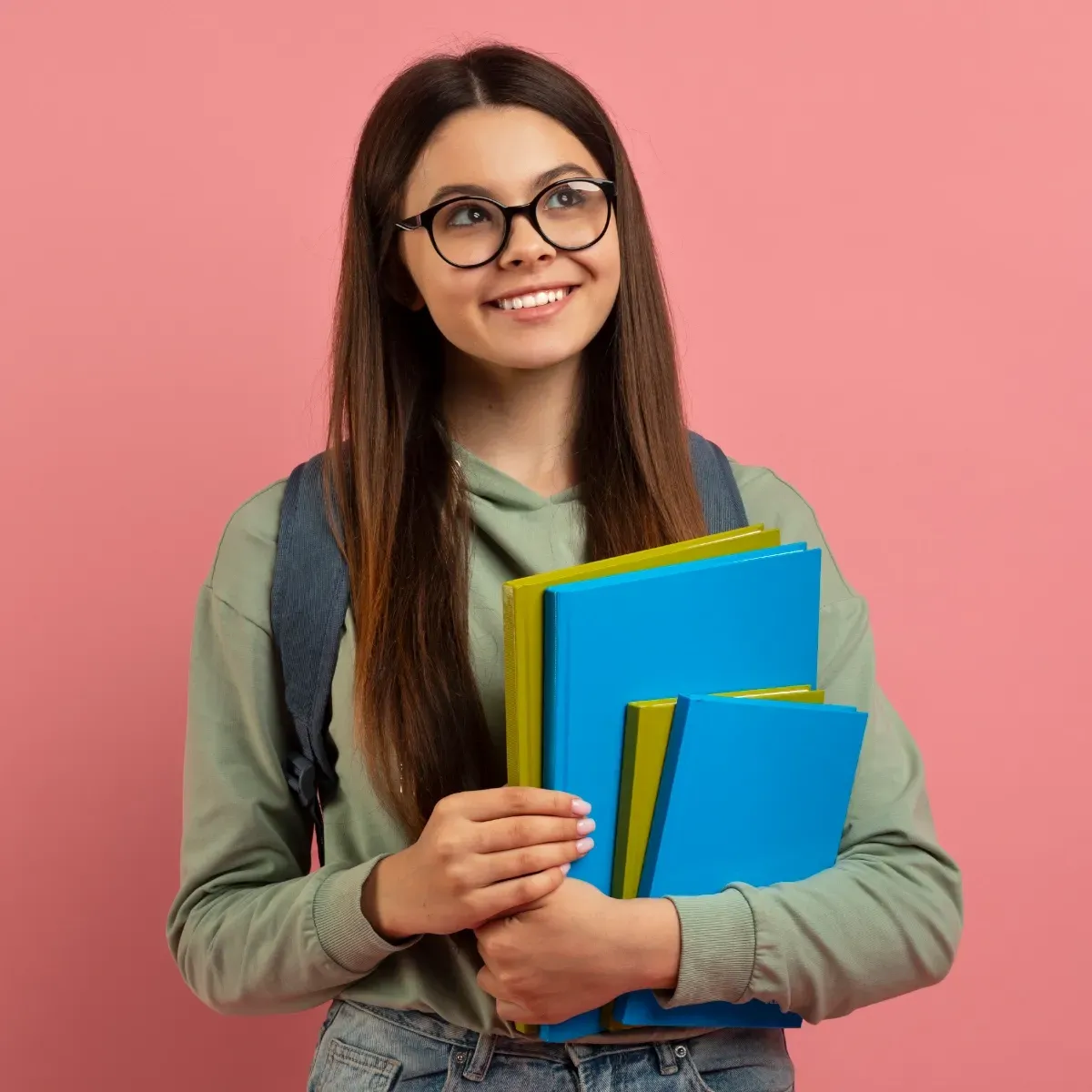 A young woman wearing glasses is holding a stack of books.