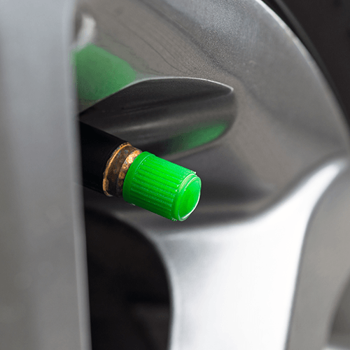 A green plastic valve stem cap on a car tire, signaling the tire is filled with nitrogen.