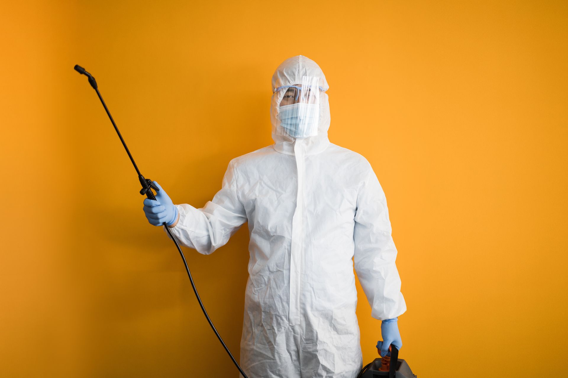 young man in protective suit disinfects on orange backgrounds young man in protective suit disinfects on orange backgrounds