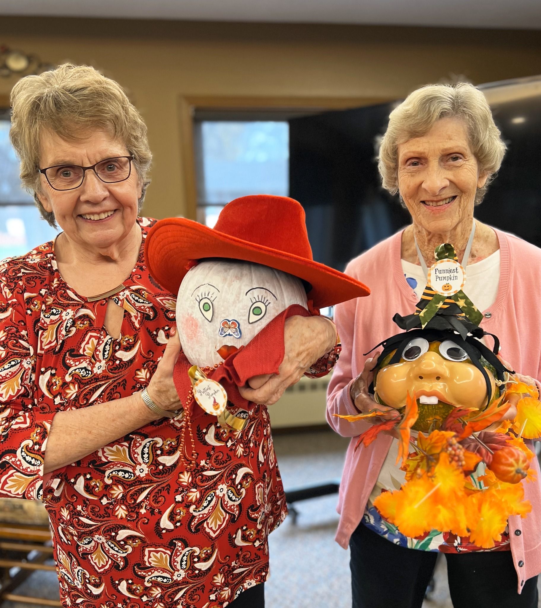 Two older women are holding a scarecrow and a pumpkin.