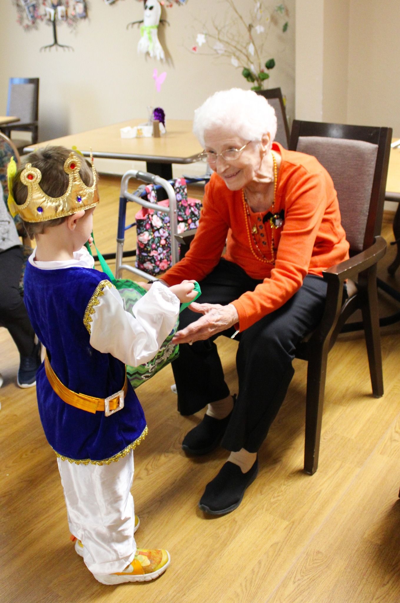 A little boy in a king costume is giving an elderly woman a gift.