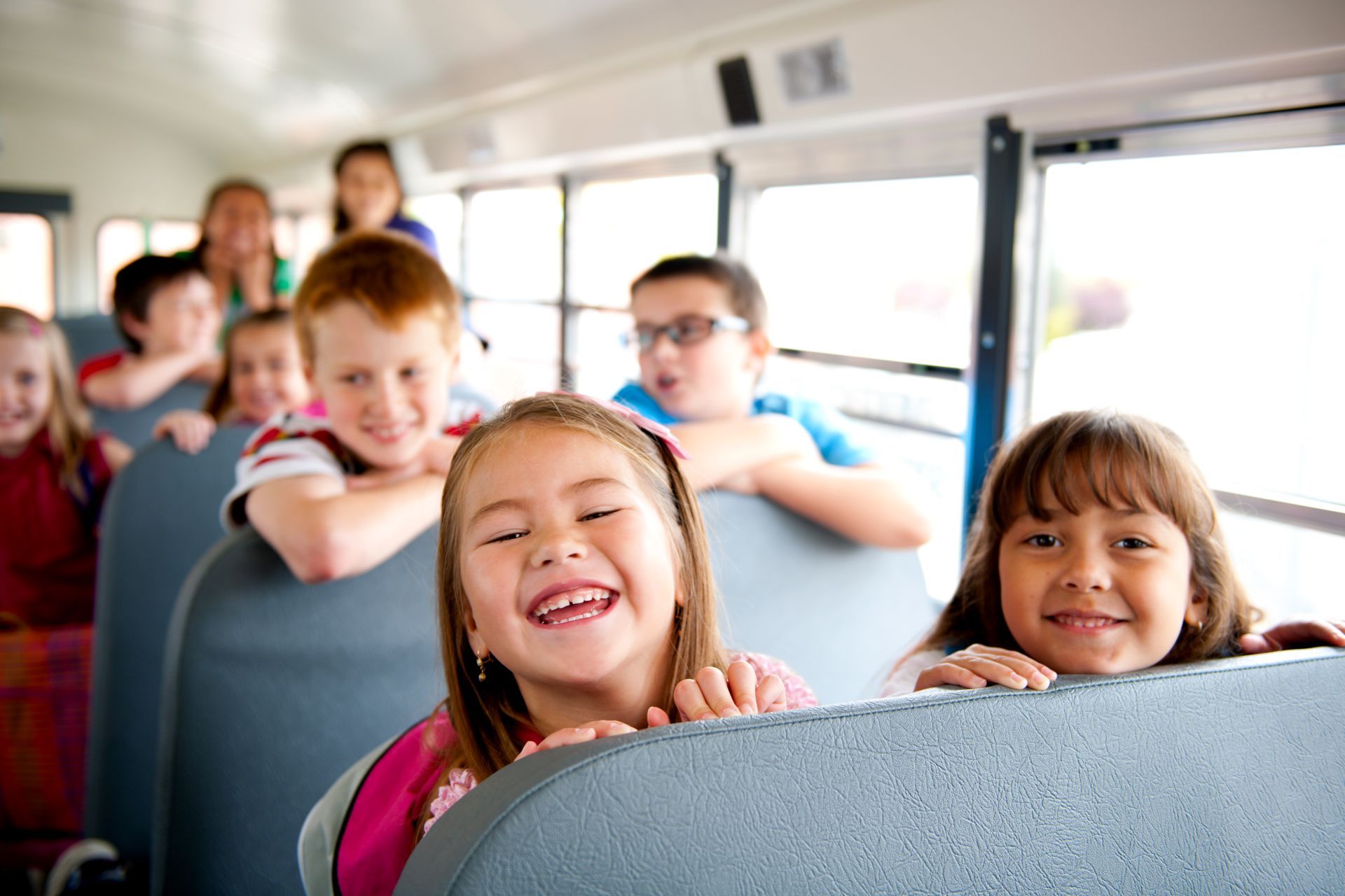 A group of children are sitting on a school bus and smiling.