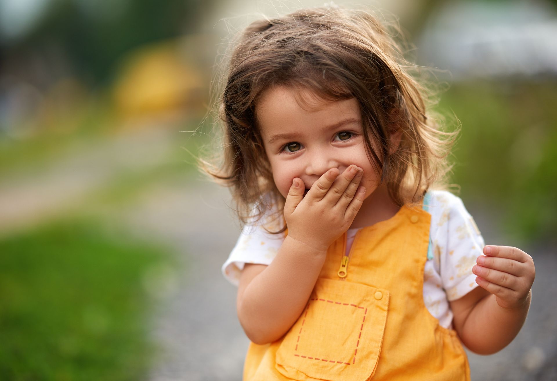 A little girl is covering her mouth with her hands and smiling.