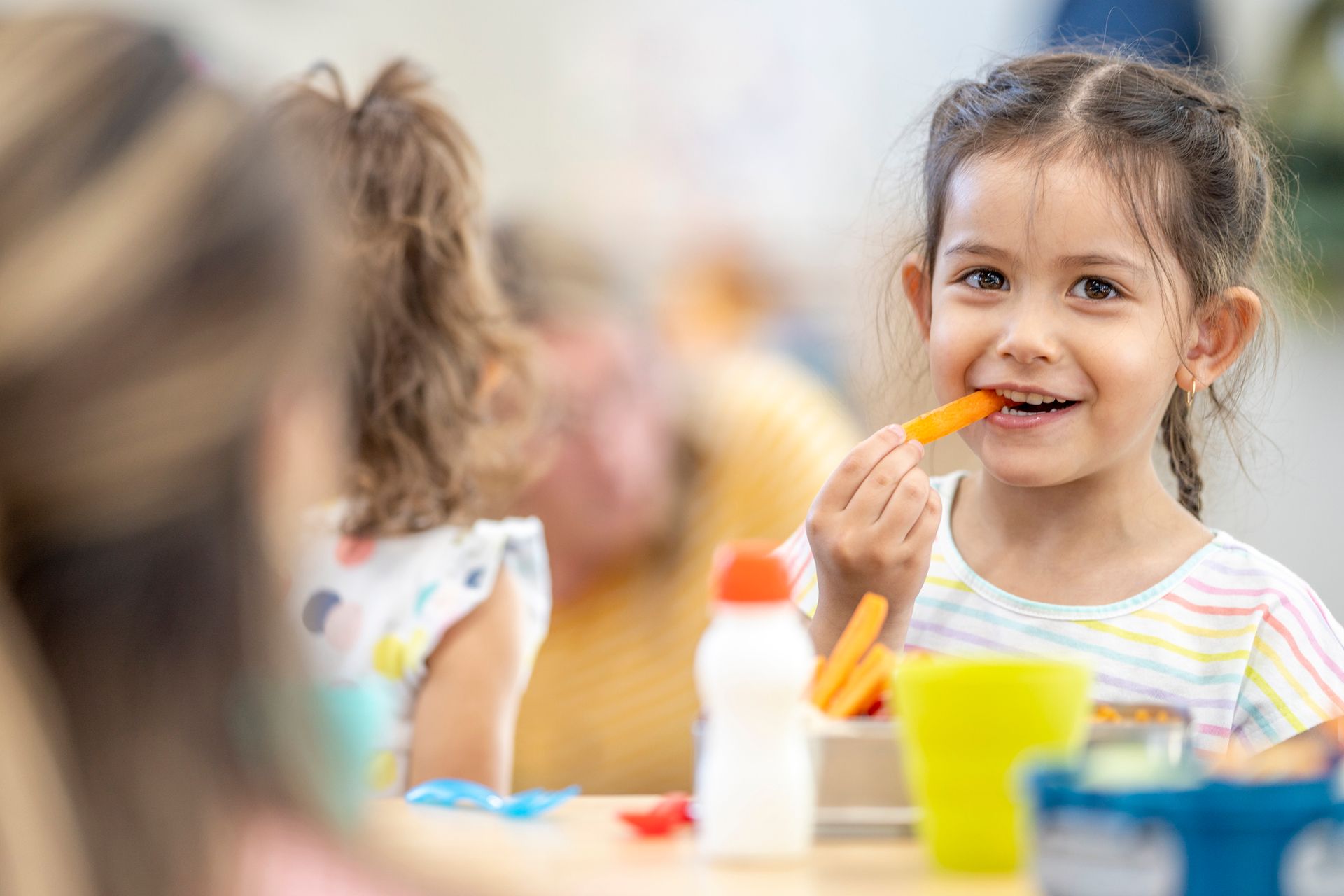 A little girl is sitting at a table eating carrots.