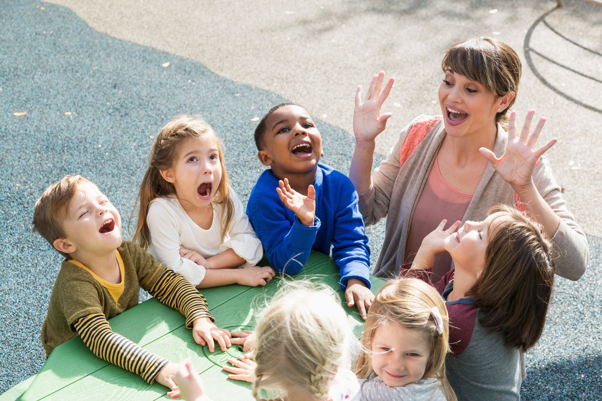 A group of children are sitting around a table with a teacher.