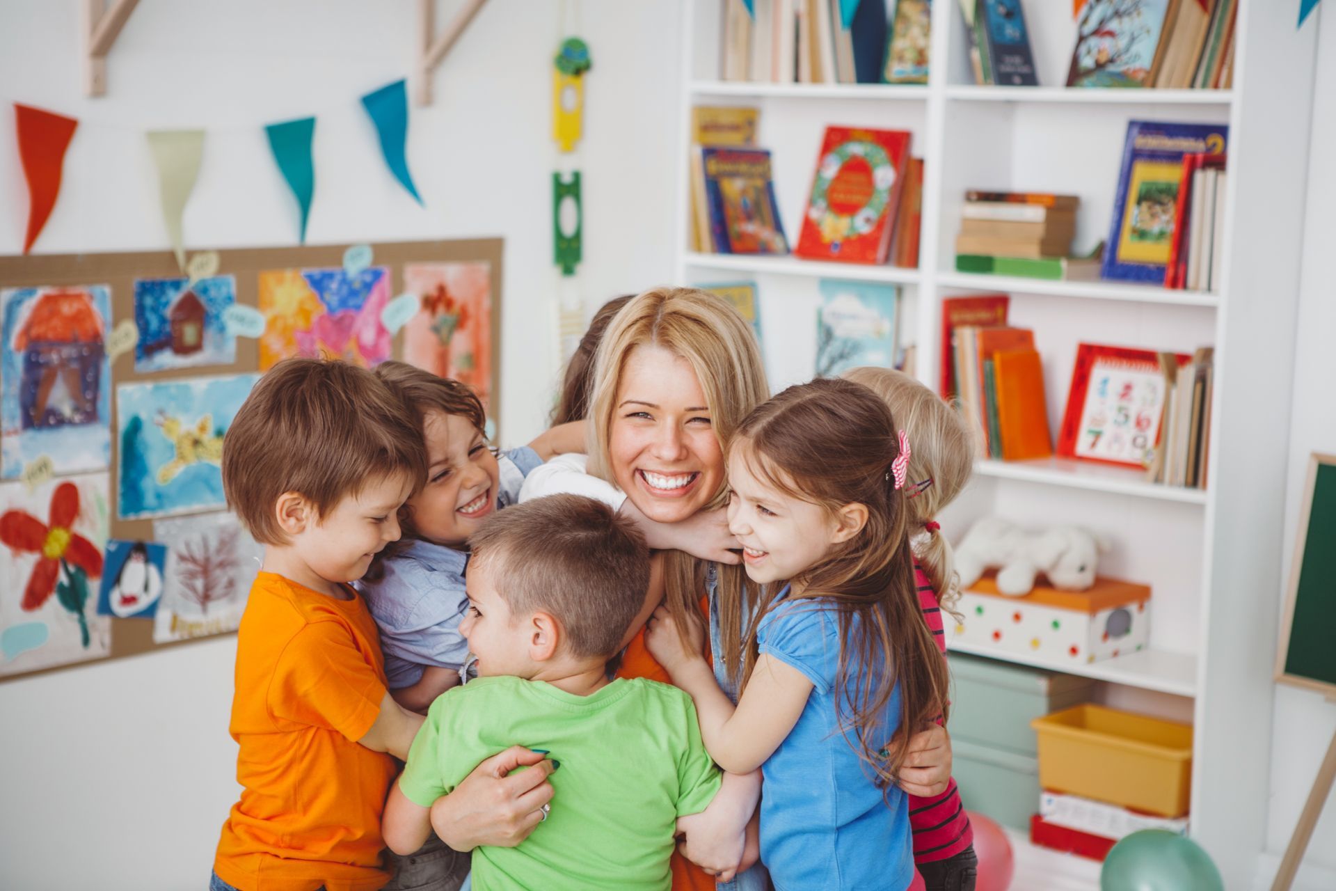 A group of children are hugging their teacher in a classroom.