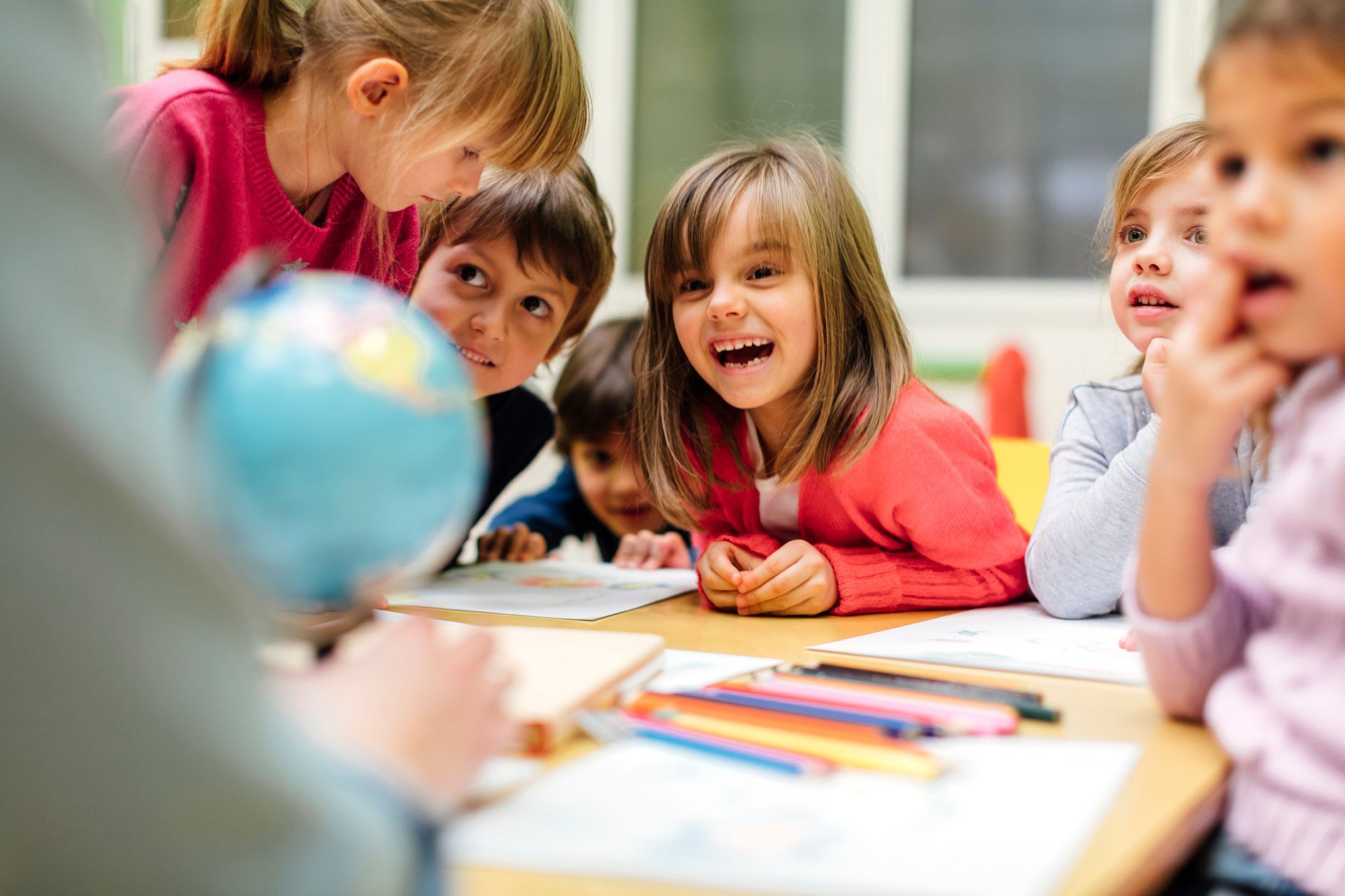 A group of children are sitting around a table looking at a globe.