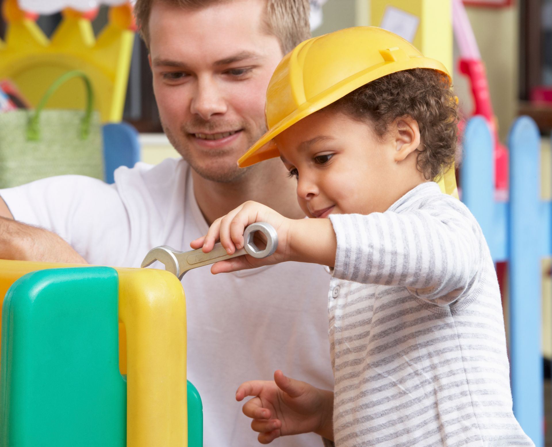 A little boy wearing a hard hat is playing with a wrench with his father